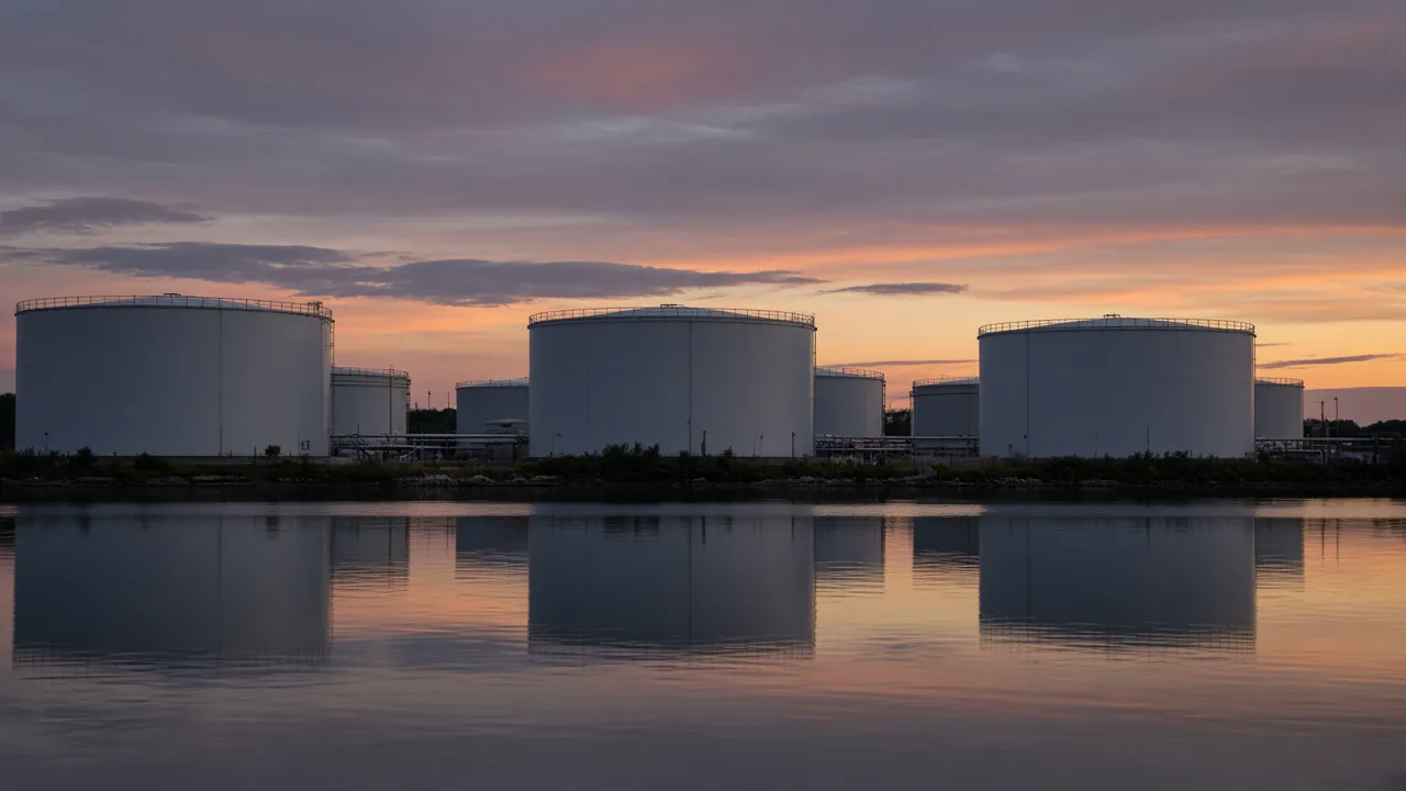 Unbranded cylindrical storage tanks beside still water at dusk, with no lettering and no people