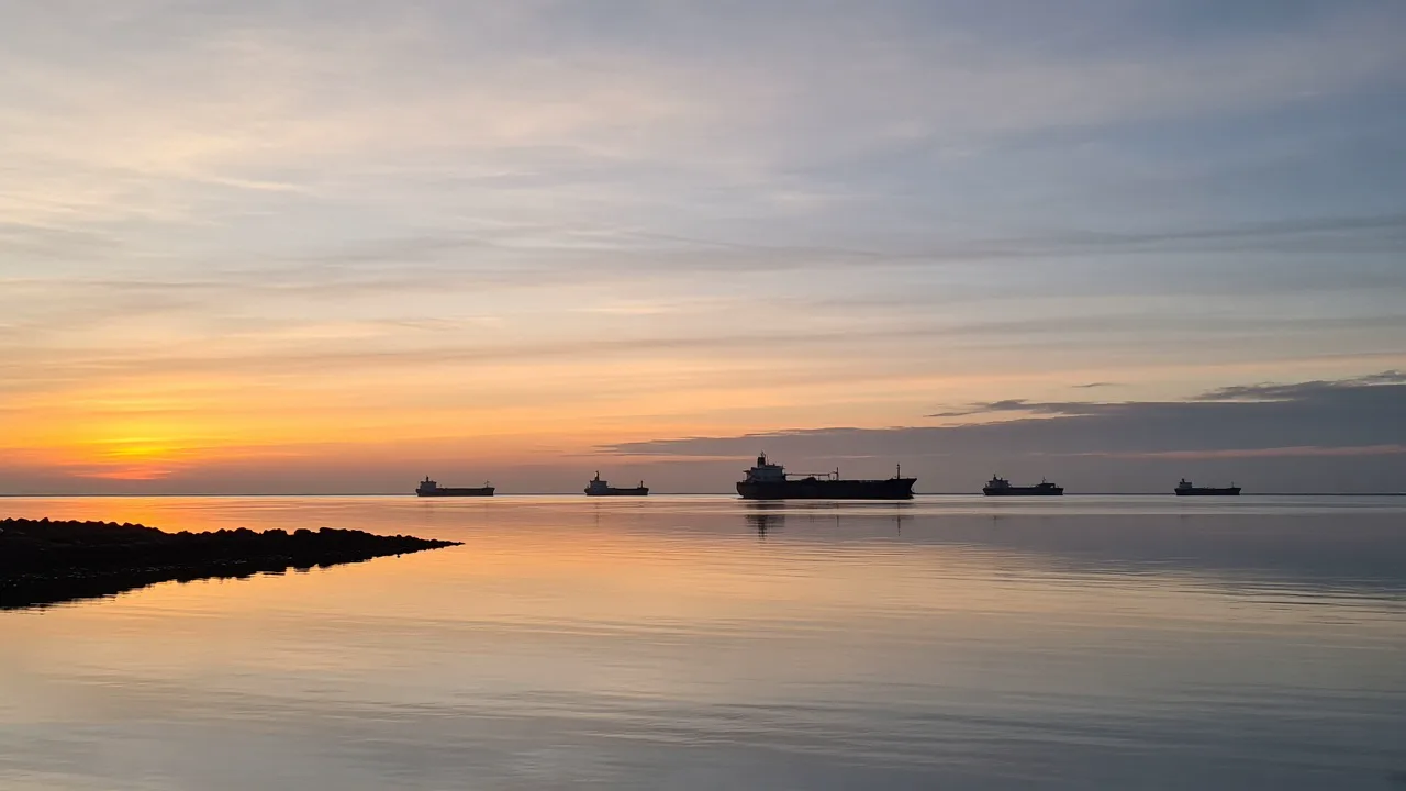 Quiet harbor at dawn with distant tankers whose hulls show no readable names, and no people in the foreground
